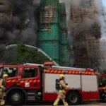 Bomberos trabajan entre el humo y los restos del andamiaje colapsado en el complejo afectado de Tai Po.