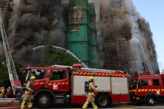Bomberos trabajan entre el humo y los restos del andamiaje colapsado en el complejo afectado de Tai Po.