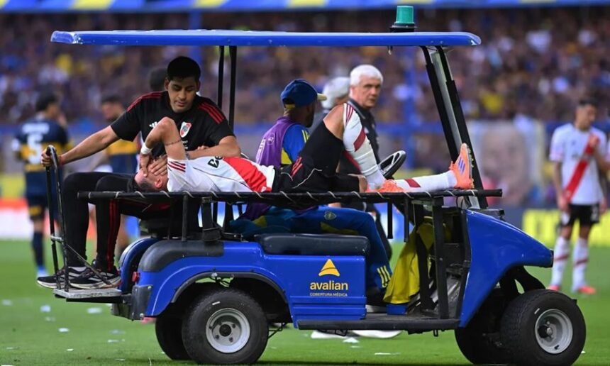 Maxi Meza es retirado del campo con visibles gestos de dolor tras sufrir la lesión en el Superclásico ante Boca.