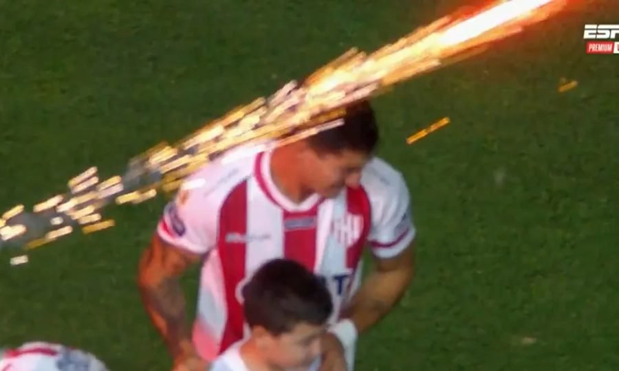 Momento en que un artefacto pirotécnico sale en dirección horizontal durante la formación del equipo, cerca del jugador Valentín Fascendini.