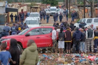Vecinos y testigos permanecen en estado de conmoción en las inmediaciones de la taberna de Bekkersdal, mientras fuerzas de seguridad trabajan en la escena tras el ataque armado ocurrido durante la madrugada.