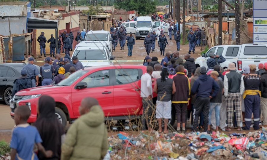 Vecinos y testigos permanecen en estado de conmoción en las inmediaciones de la taberna de Bekkersdal, mientras fuerzas de seguridad trabajan en la escena tras el ataque armado ocurrido durante la madrugada.