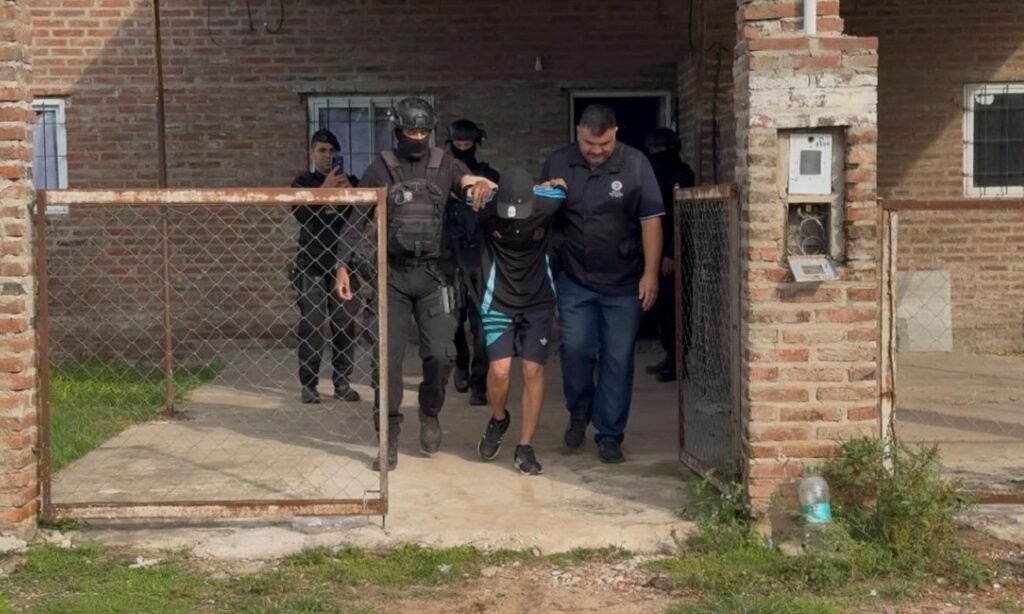 Momento en que personal de la PDI traslada a uno de los detenidos tras los allanamientos por el homicidio investigado. Foto: archivo.