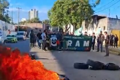 Manifestación de trabajadores municipales con corte de tránsito y quema de cubiertas en una avenida urbana.