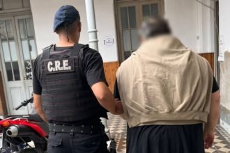 Hombre de 66 años detenido y trasladado a sede policial en la ciudad de Santa Fe, escoltado por efectivos tras ser acusado de amenazar a su familia.