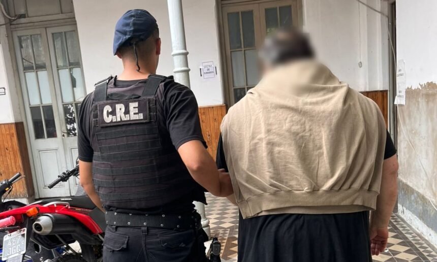 Hombre de 66 años detenido y trasladado a sede policial en la ciudad de Santa Fe, escoltado por efectivos tras ser acusado de amenazar a su familia.