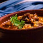 Plato de locro argentino tradicional preparado con carnes, maíz blanco, porotos y zapallo.